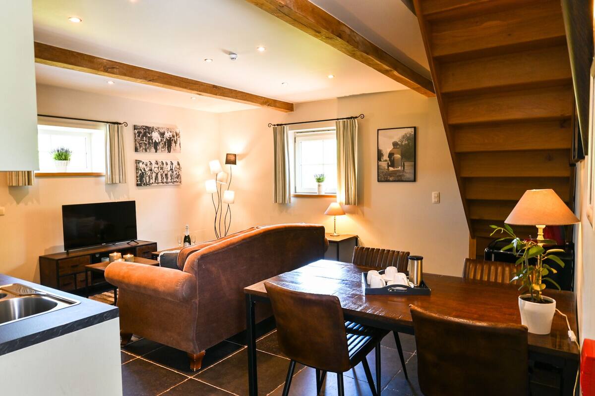 Uma sala de estar aconchegante com televisão, um sofá, uma mesa de jantar e uma área de cozinha com pia.