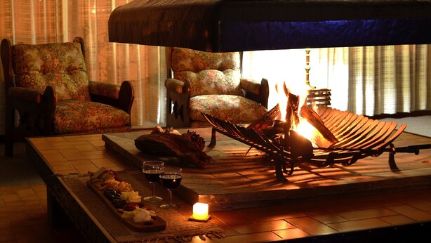 A cozy lounge area with a wooden bench, a floral armchair, and a small table with snacks and drinks. - Hosteria Güemes (San Carlos de Bariloche)