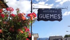 A sign for 'Hosteria Guemes' with a backdrop of blooming flowers and a clear sky. - Hosteria Güemes (San Carlos de Bariloche)
