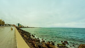 Un paseo marítimo con sendero de hormigón, costa rocosa y edificios al fondo.