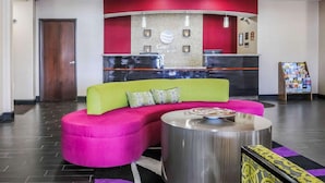 A reception area with a curved desk, a sofa with pillows, a coffee table, and a magazine rack. - Comfort Inn & Suites West Artesia (Artesia)