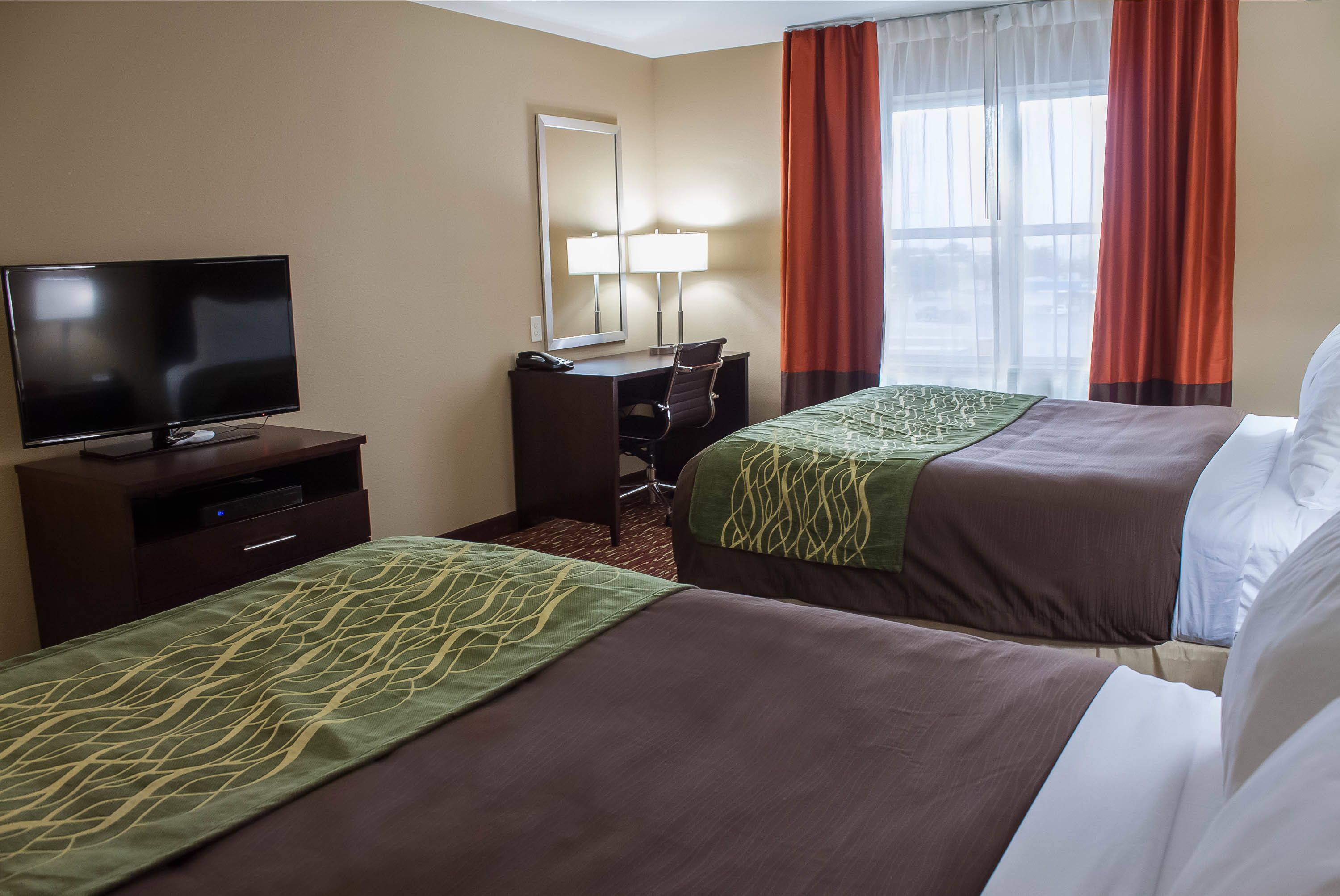 Habitación de hotel con dos camas, un escritorio con silla, televisión y ventana con cortinas.