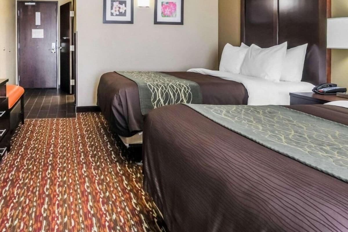 A hotel room with two beds, a desk with a lamp, and a door leading to another room.
