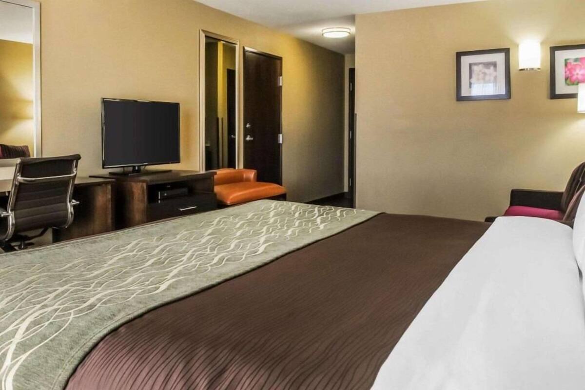 Una habitación de hotel con una cama grande, un escritorio con televisión, una silla naranja y una puerta que da a otra habitación.