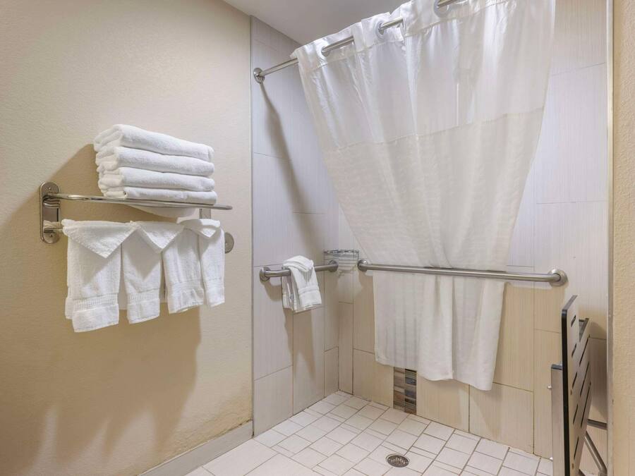 Un espacio de ducha con cortina blanca, un perchero con toallas dobladas y una barra de apoyo.
