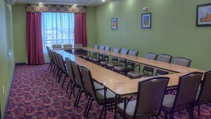 A conference room with a long table and chairs, a patterned carpet, and a window with curtains. - Comfort Inn & Suites West Artesia (Artesia)
