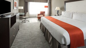 Een hotelkamer met een groot bed, een bureau met een televisie, een stoel en een raam met gordijnen.