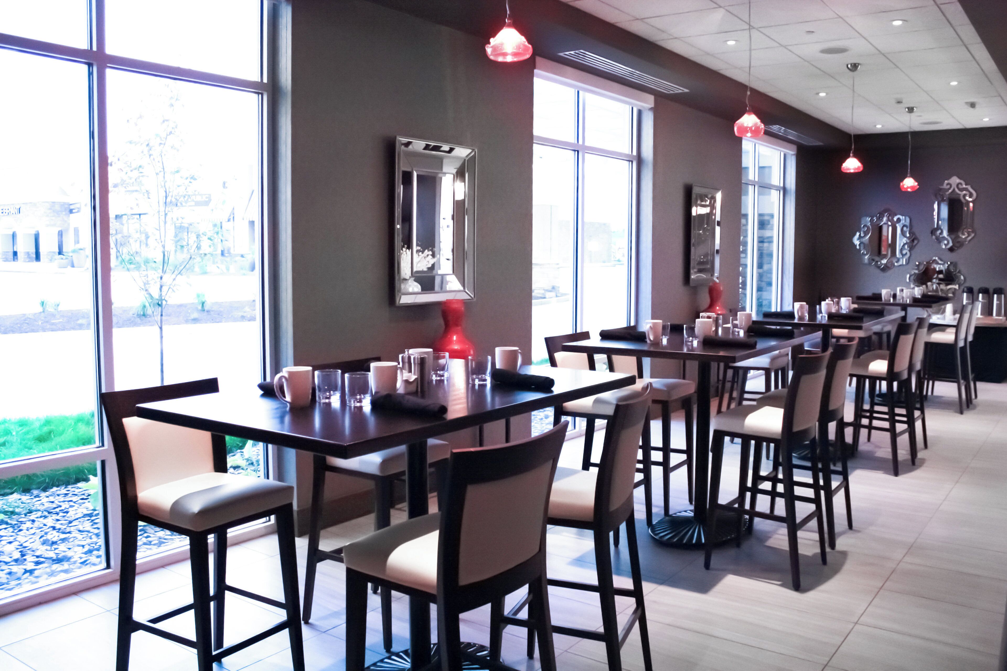 Un restaurante con varias mesas y sillas, ventanas amplias e iluminación colgante.