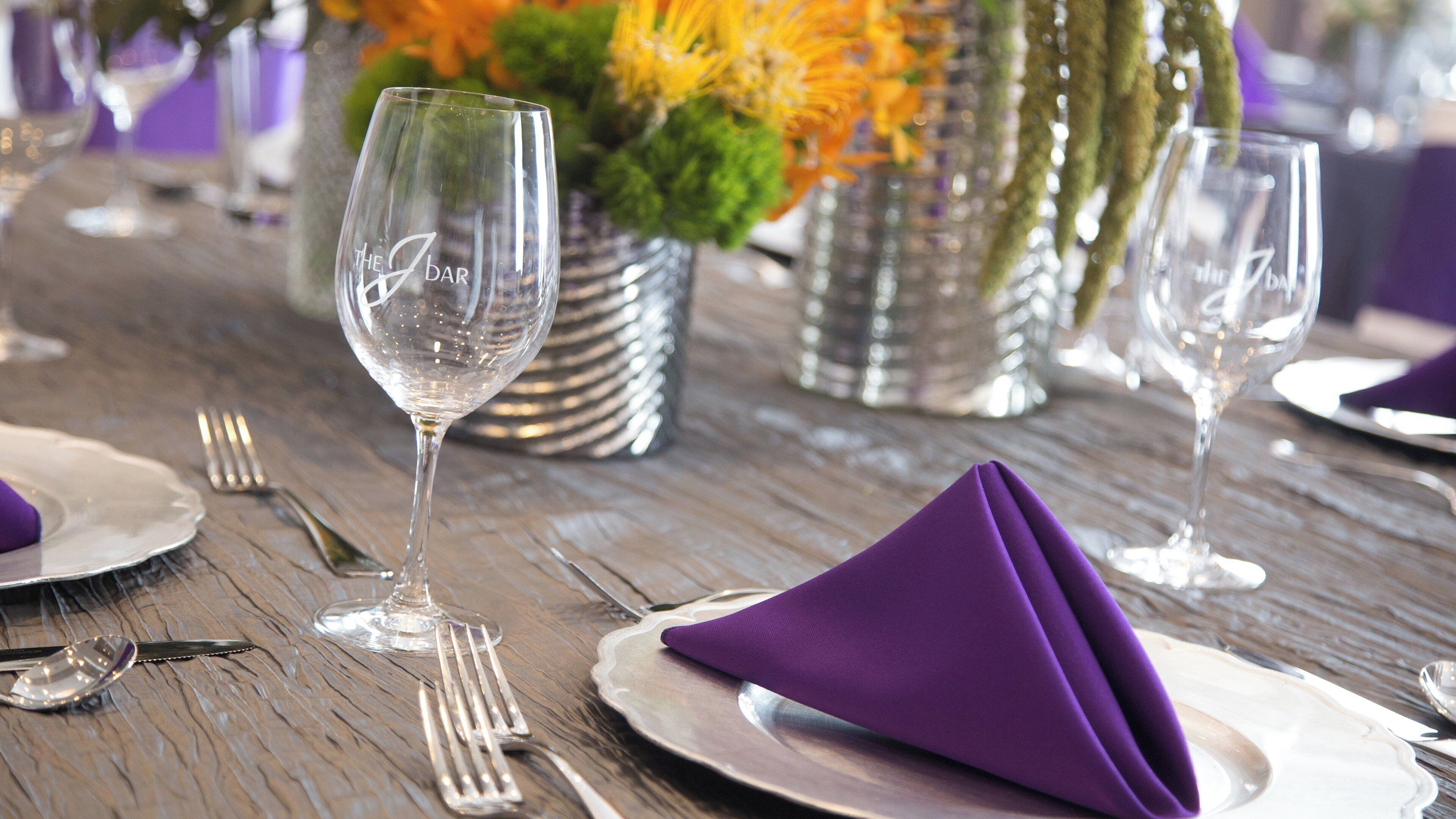 Una mesa dispuesta con copas de vino, cubiertos y un mantel individual morado.