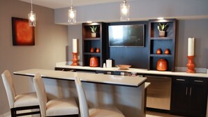 A modern kitchen with a central island, bar stools, pendant lighting, and built-in shelving with decorative items. - Holiday Inn Hotel & Suites Davenport by IHG (Davenport)