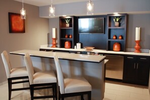 Une cuisine moderne dotée d’un îlot central, de tabourets de bar, de luminaires suspendus et d’étagères intégrées où sont exposés des objets décoratifs.