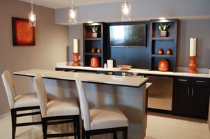 Una cocina moderna con una isla central, taburetes de bar, iluminación colgante y estanterías empotradas con objetos decorativos.