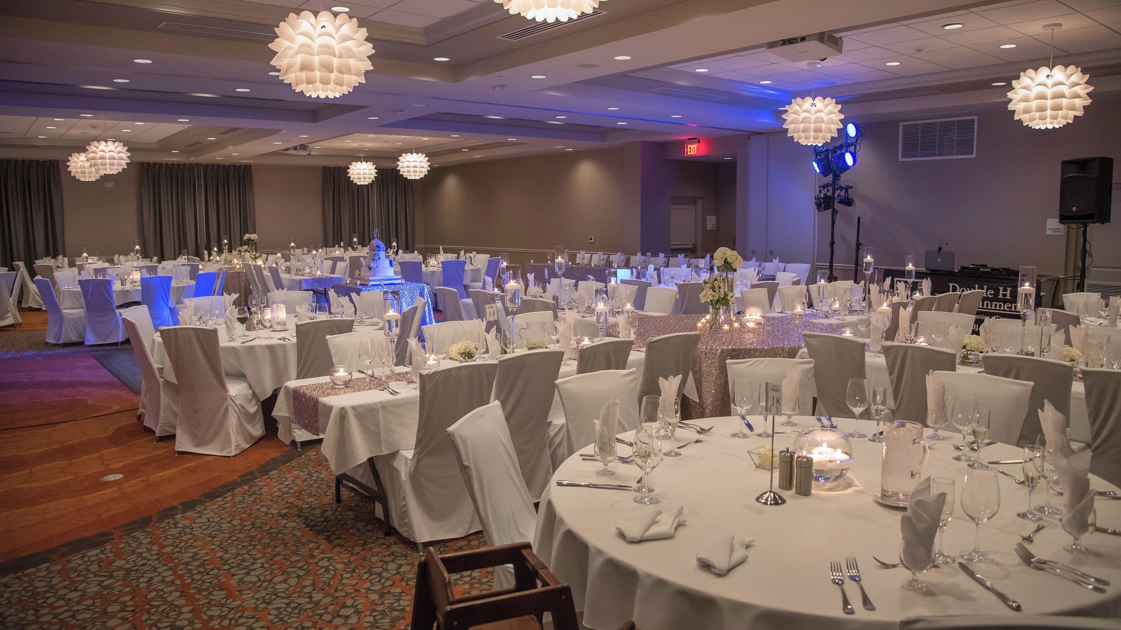 Een balzaal met ronde tafels gedekt voor een formeel evenement, met witte tafelkleden, stoelen en decoraties.
