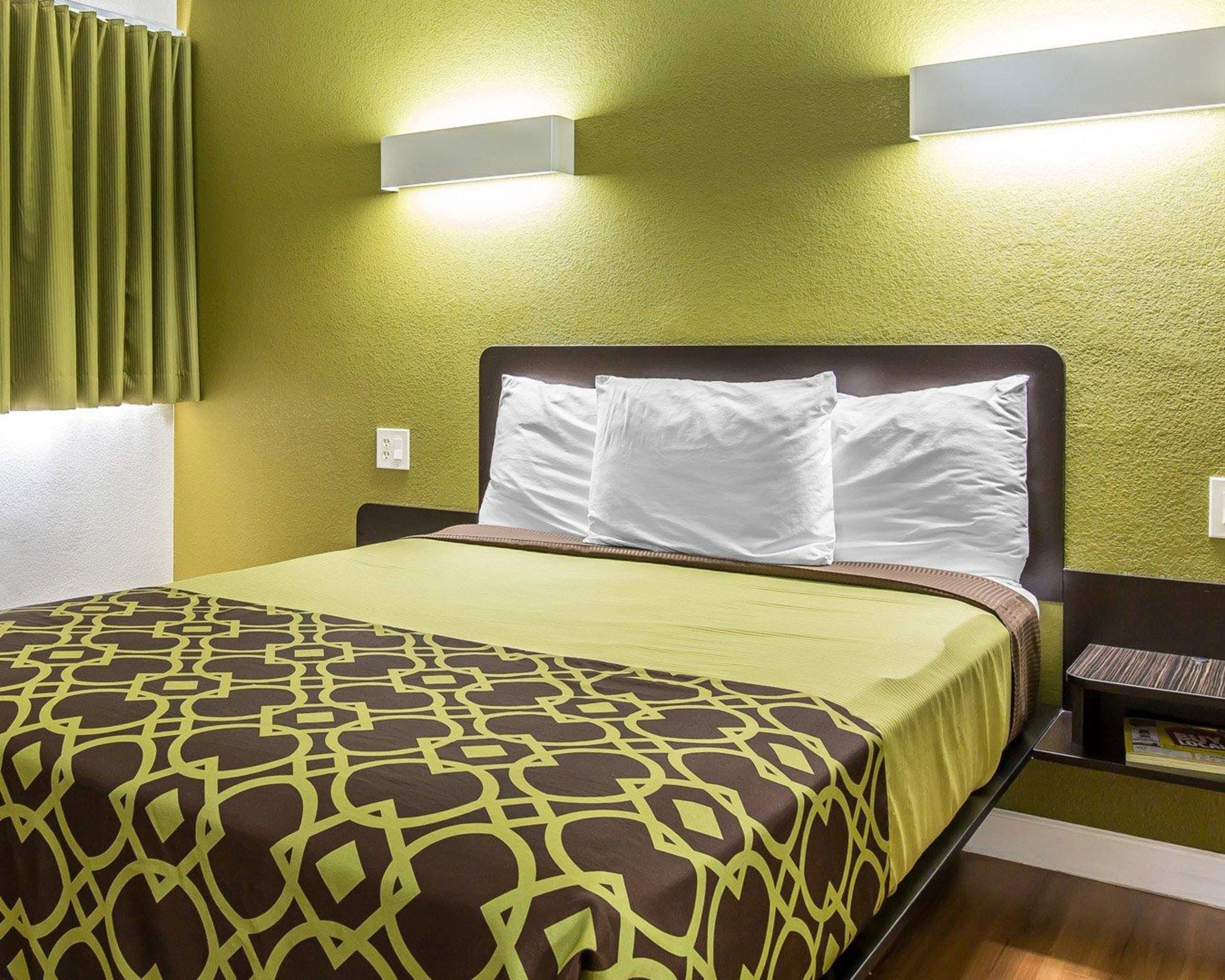 Habitació d'hotel amb un llit, parets verdes i dues làmpades penjades a la paret.