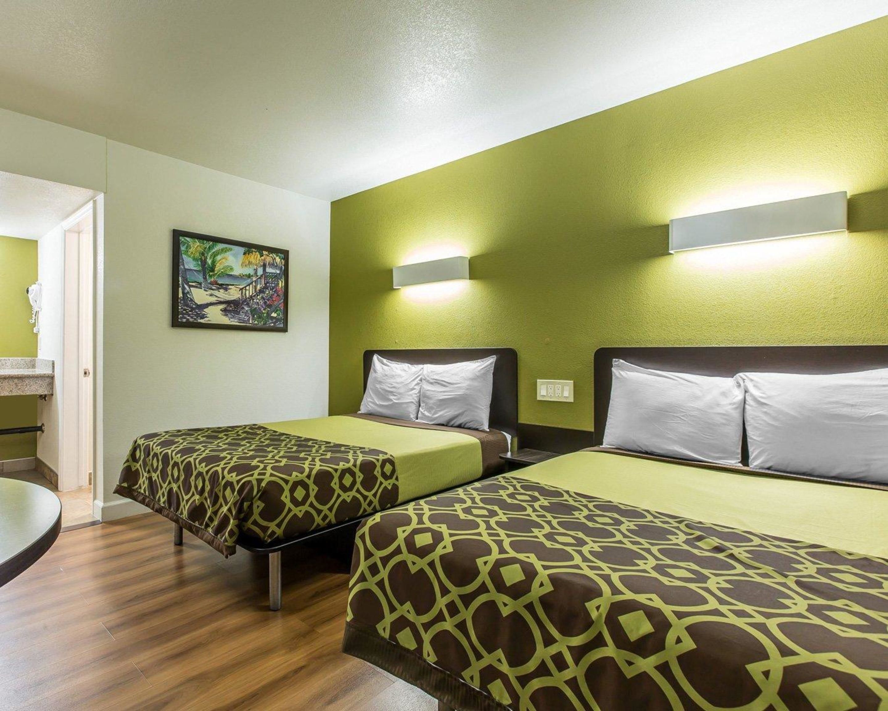 Una habitación de hotel con dos camas, un cuadro en la pared y un baño visible a través de una puerta abierta.