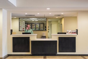 A reception desk with a receptionist, a decorative wall, and a reception counter. - Candlewood Suites Bloomington by IHG (Bloomington)