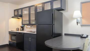 Una cocina compacta con muebles oscuros, un refrigerador empotrado, estufa y una pequeña mesa de comedor con una silla.
