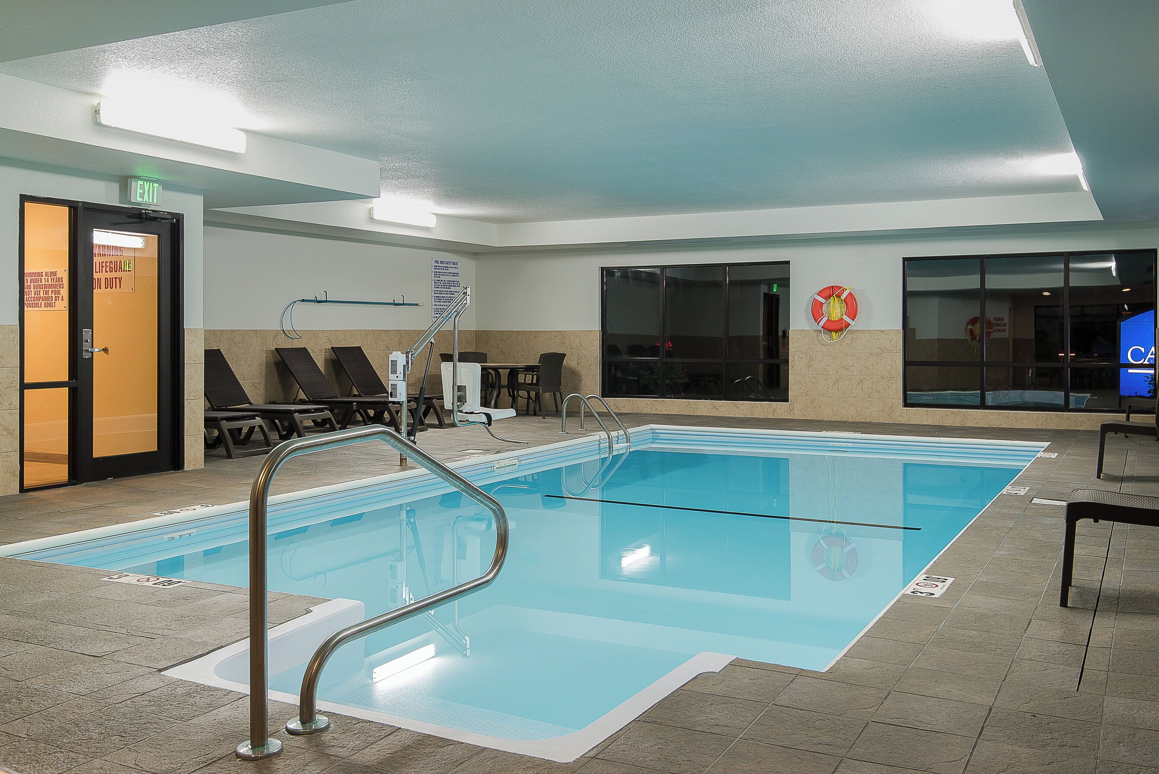 Une piscine intérieure équipée d’un poste de surveillance pour le sauveteur, de chaises longues et d’un escalier pour accéder à la piscine.
