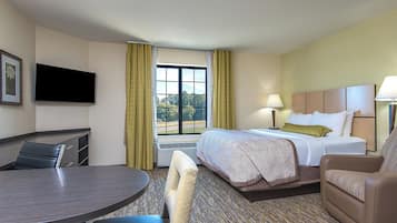Habitación de hotel con cama, escritorio, silla, televisor y ventana con cortinas.