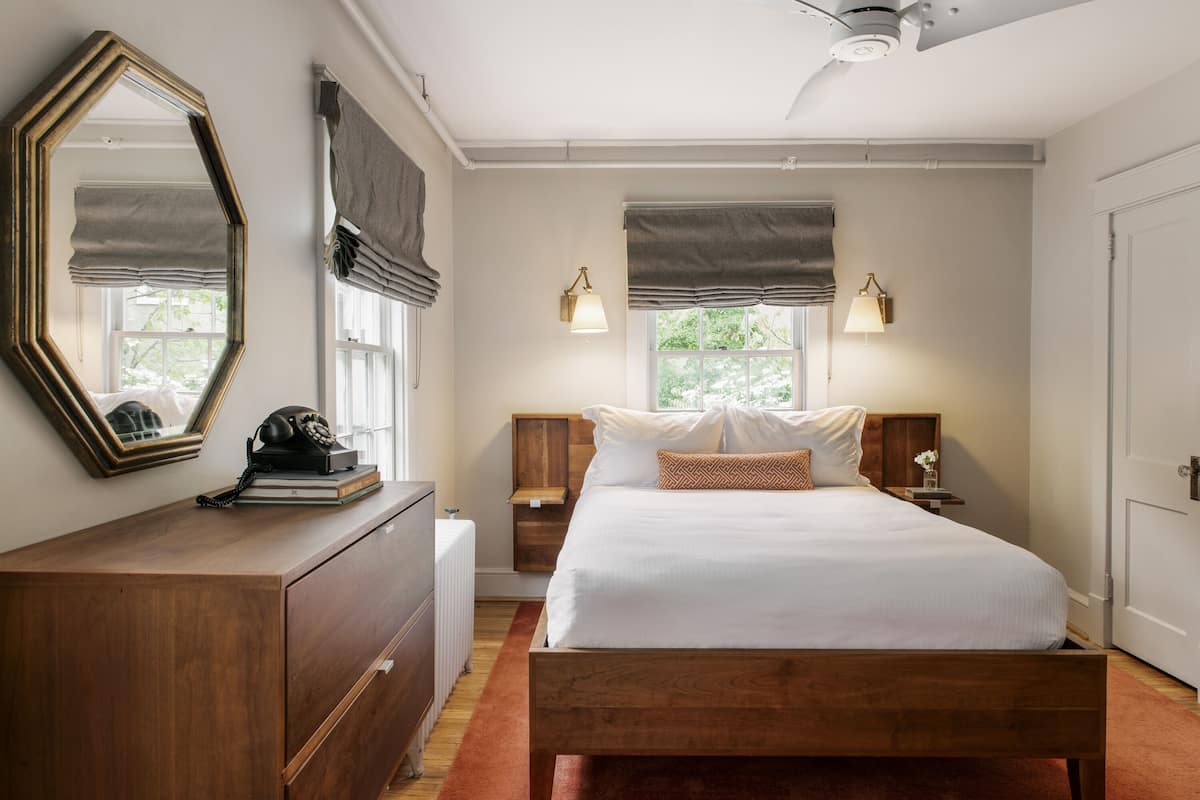 A bedroom with a wooden bed, a dresser, a mirror, two bedside lamps, and a ceiling fan.