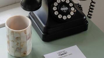 Un teléfono antiguo de disco giratorio negro, una taza de cerámica con estampado floral, un bloc de notas con el texto
