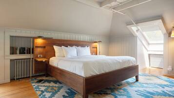 A bedroom with a wooden bed, white bedding, a patterned rug, a skylight, and a radiator.