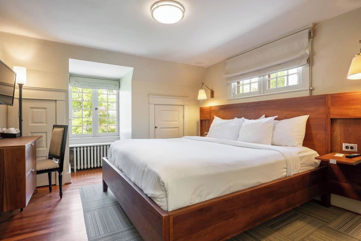 A bedroom with a wooden bed, a desk, a chair, and a window with a view.