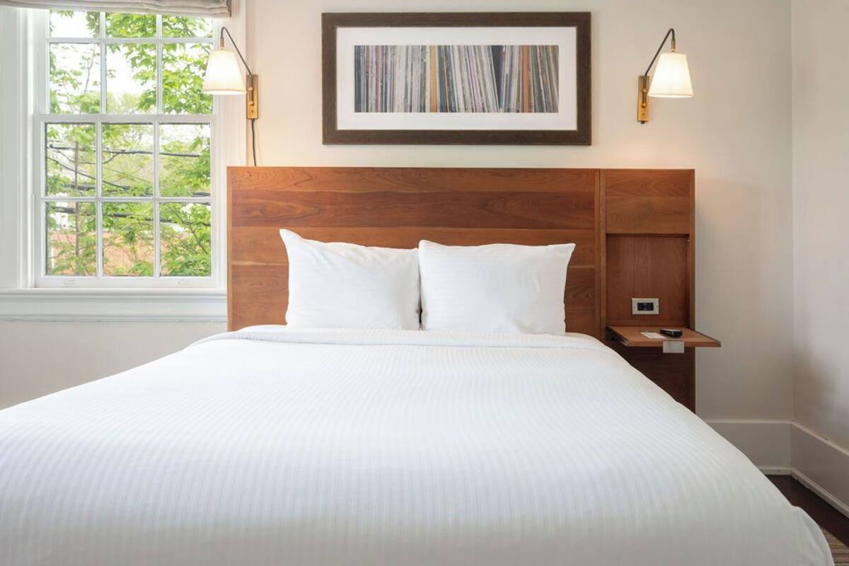A neatly made bed with white linens, a wooden headboard, and a bedside table with a lamp.