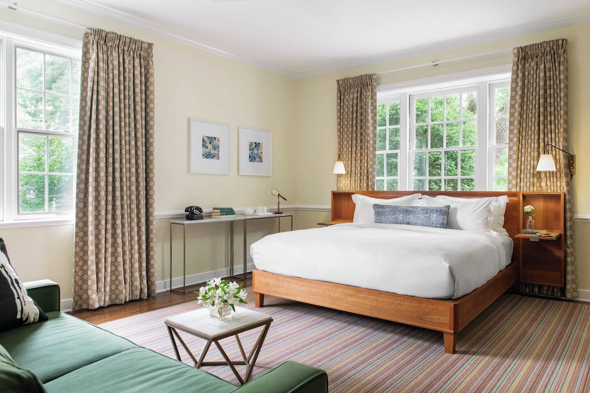 A bedroom with a large bed, a desk, a green sofa, and a window with curtains.