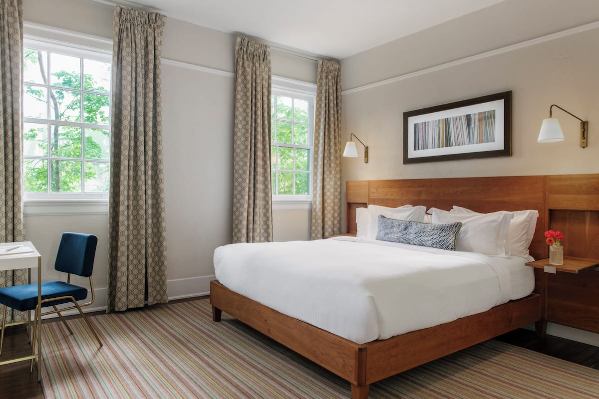 A hotel room with a large bed, a desk, a chair, and a window with curtains.