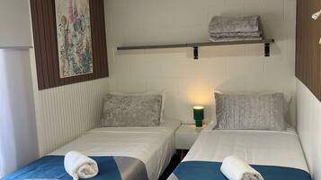A hotel room with two beds, a wall-mounted shelf with a towel, a bedside lamp, and a ceiling fan.