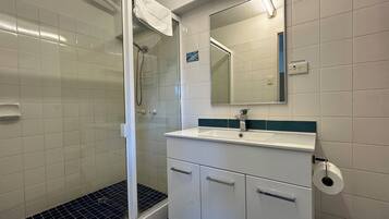 A bathroom with a shower, sink, mirror, and toilet paper dispenser.