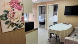 Ein Zimmer mit einem runden Tisch, einem an der Wand montierten Fernseher und einer Tür zu einem anderen Raum.