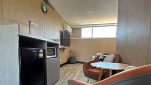 Eine kompakte Küche mit Kühlschrank, Mikrowelle und einer kleinen Essecke mit Tisch und gepolstertem Stuhl.