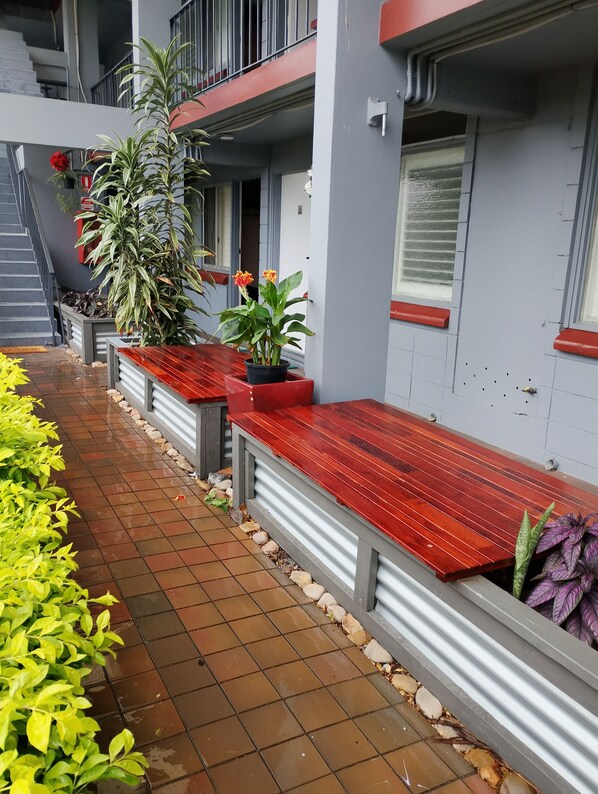 A corridor with tiled flooring, red benches, potted plants, and a staircase. - Airway Motel (Ascot)