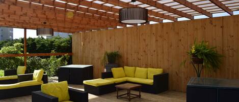 Un patio al aire libre con suelo de madera, mobiliario amarillo y negro, y estructura de techo de madera.