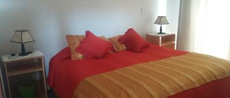 A bed with a red and beige striped bedspread, two red pillows, and a wooden nightstand with a lamp.