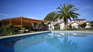 Una piscina con una pérgola de madera y una palmera al fondo.