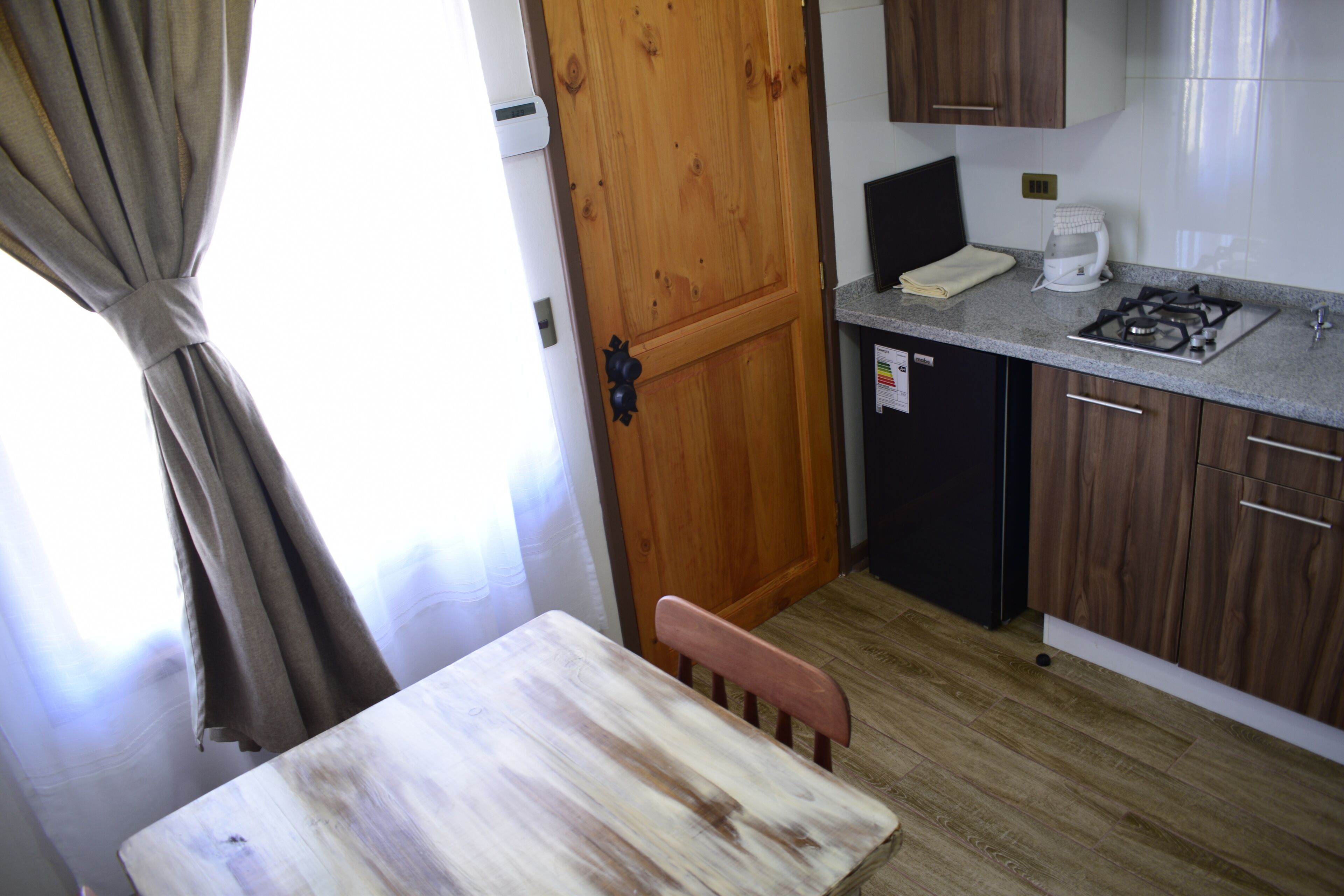 Une cuisine de taille réduite, avec des meubles de rangement en bois, une cuisinière à gaz et un petit réfrigérateur.