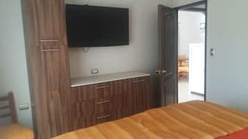 A bedroom with a bed, wooden wardrobe, and a flat-screen TV mounted on the wall.