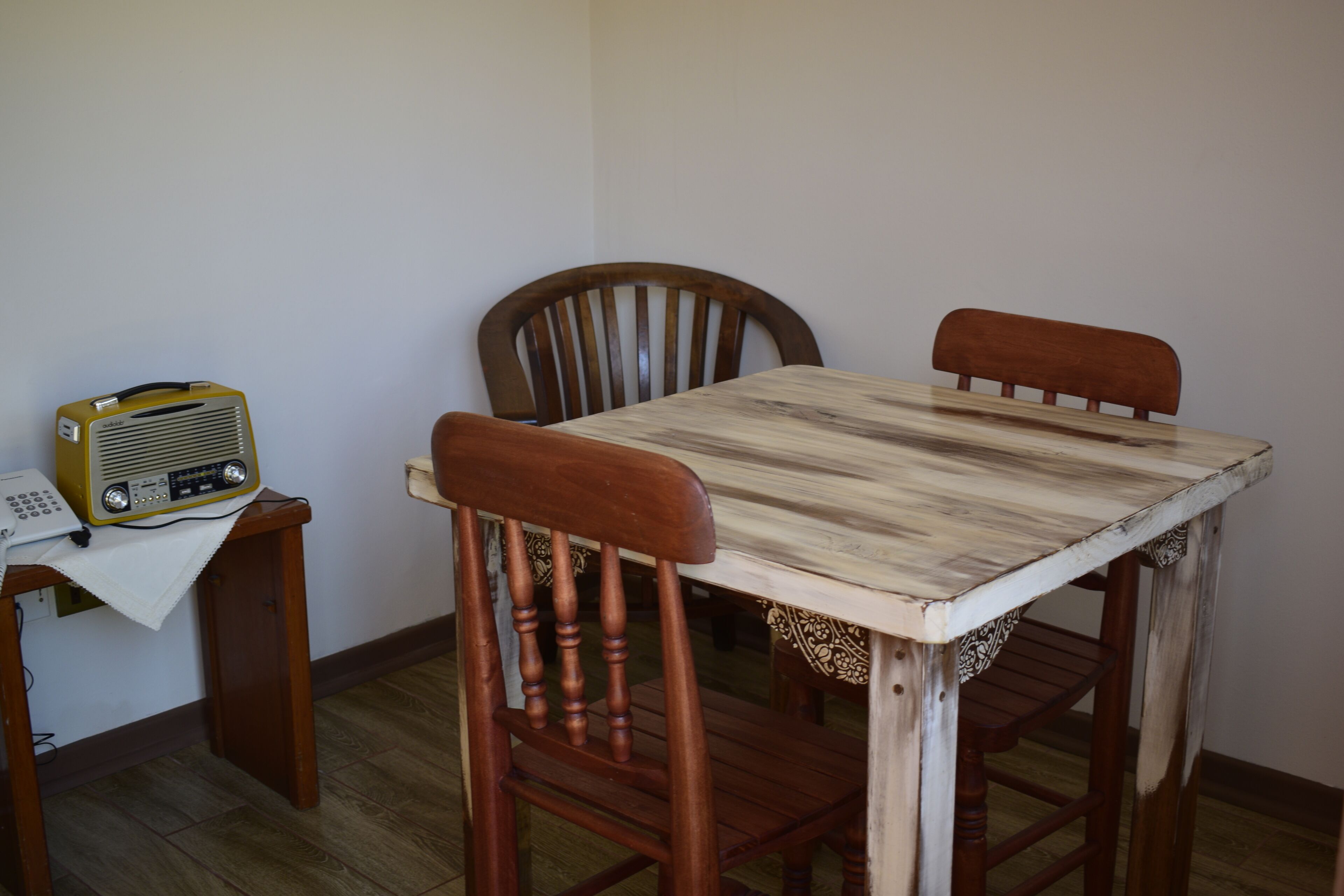 A dining table with two wooden chairs, a vintage radio on a small table, and a power outlet on the wall.