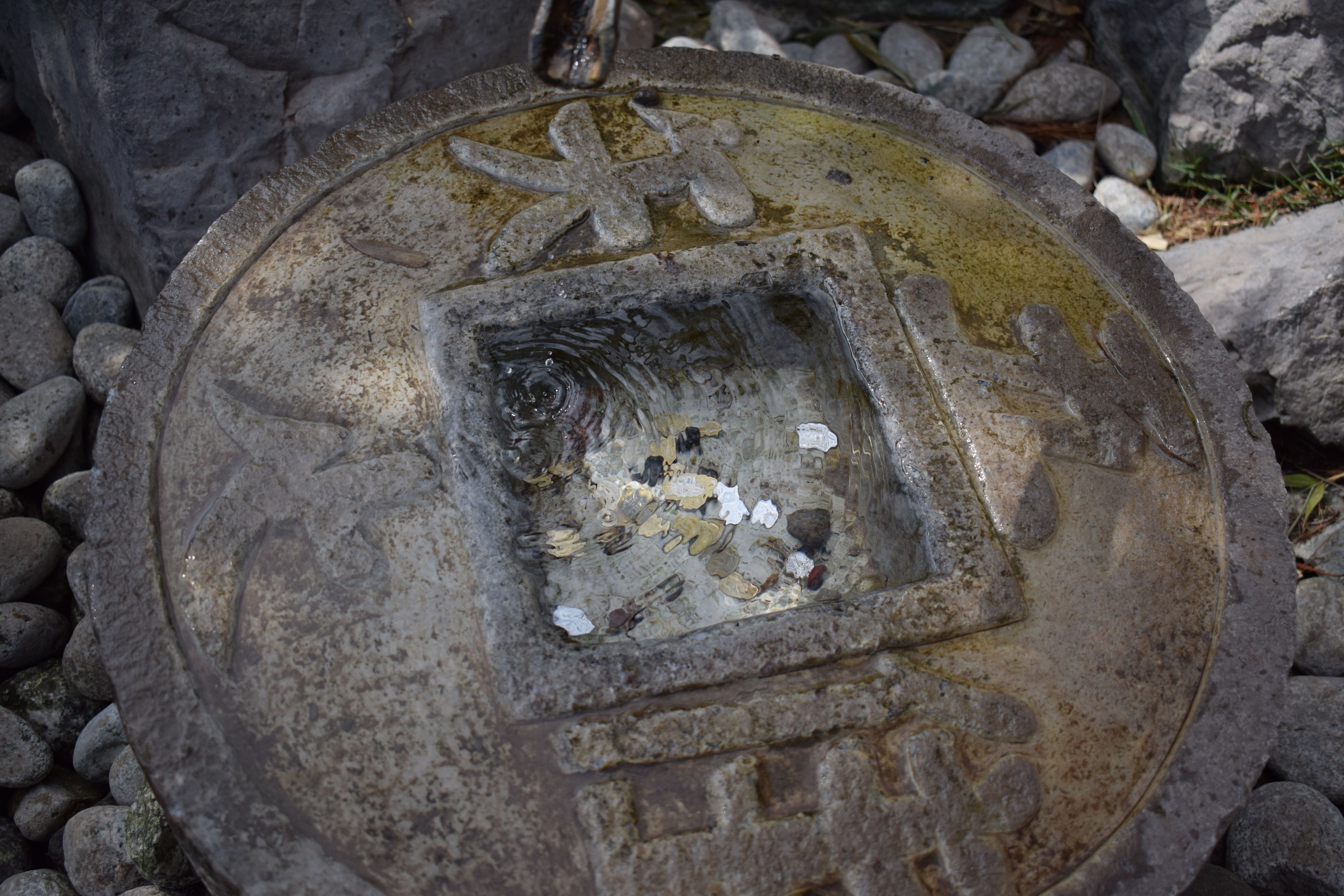 Una tapa de pozo con una abertura cuadrada, rodeada de rocas.
