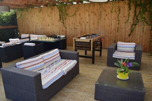 Un patio exterior con mobiliario de mimbre, una mesa de fútbol de mesa y un juego de ajedrez.