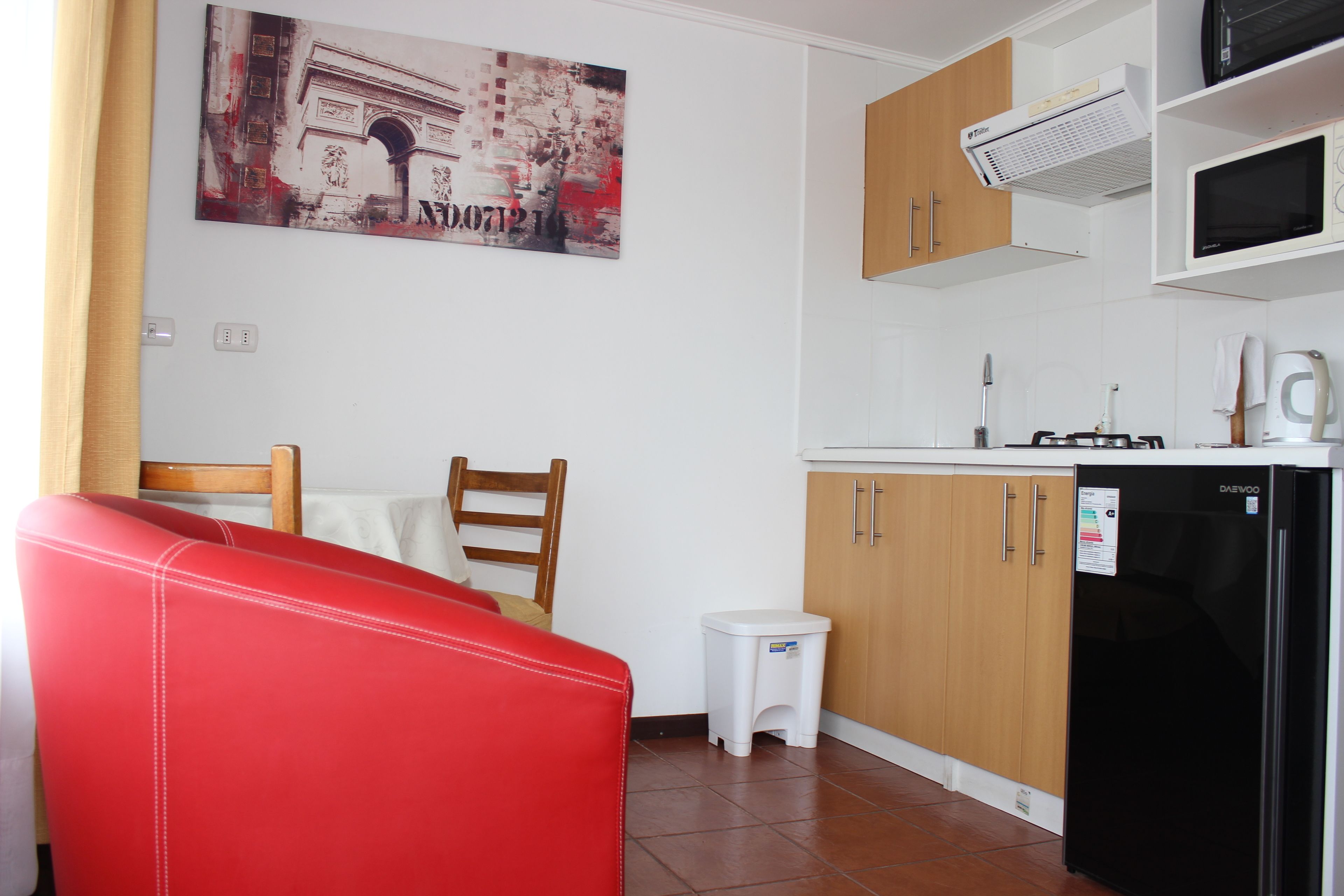 A compact kitchen with wooden cabinets, a black refrigerator, and a small white stool.