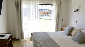 Un dormitorio con cama, cortinas, mesita de noche y vistas al exterior.