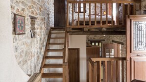 A rustic interior with a stone wall, wooden staircase, and a loft bedroom with a bed and window. - Agroktima (South Kynouria)