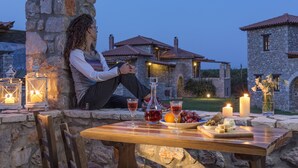 A stone wall with a table set for a meal, featuring a bottle, glasses, and a plate of cheese and grapes. - Agroktima (South Kynouria)