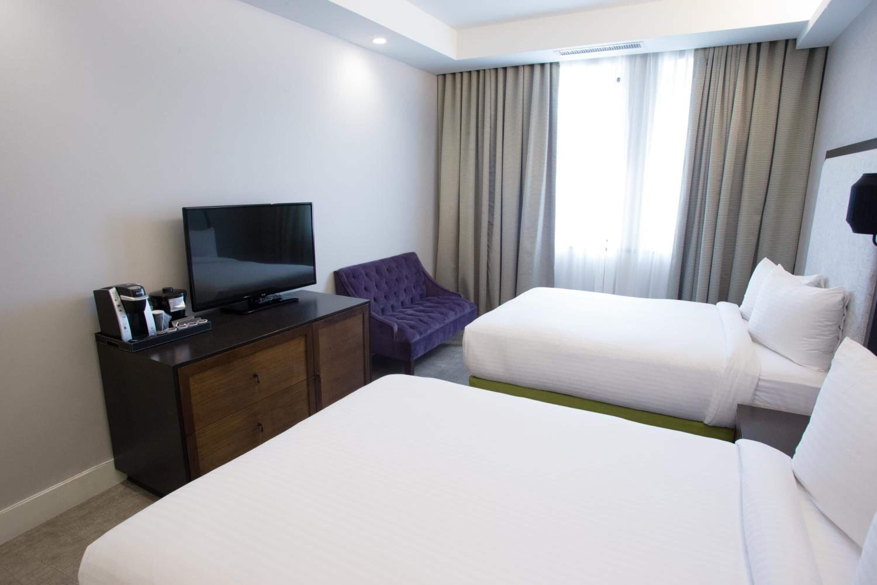 Une chambre d’hôtel avec deux lits, une télévision, une commode et une fenêtre avec des rideaux.