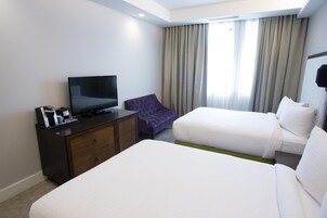 A hotel room with two beds, a TV, a dresser, and a window with curtains.