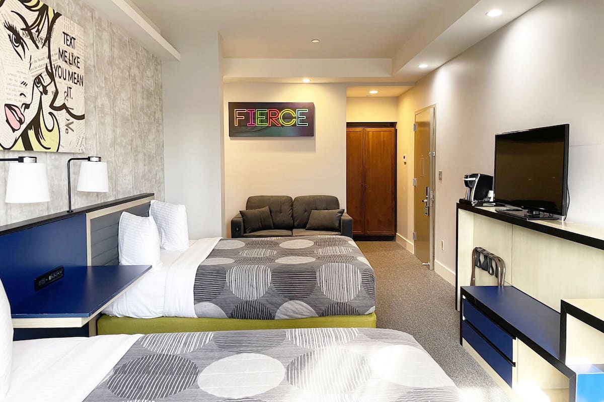 A modern hotel room with a large bed, a desk, a television, and a wardrobe.